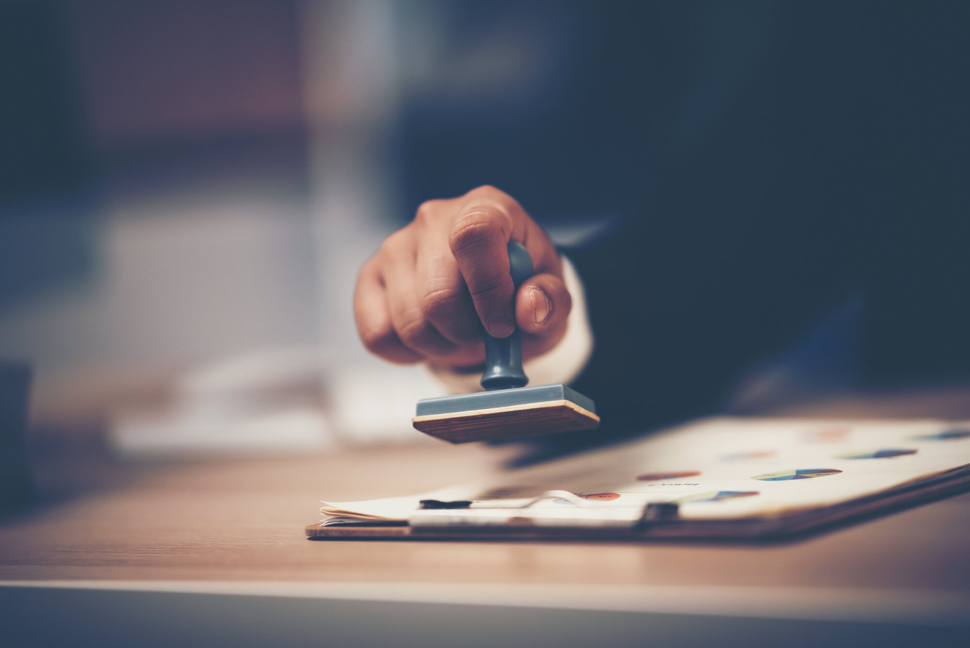 Close-up Of A Person's Hand Stamping With Approved Stamp On Document At Desk